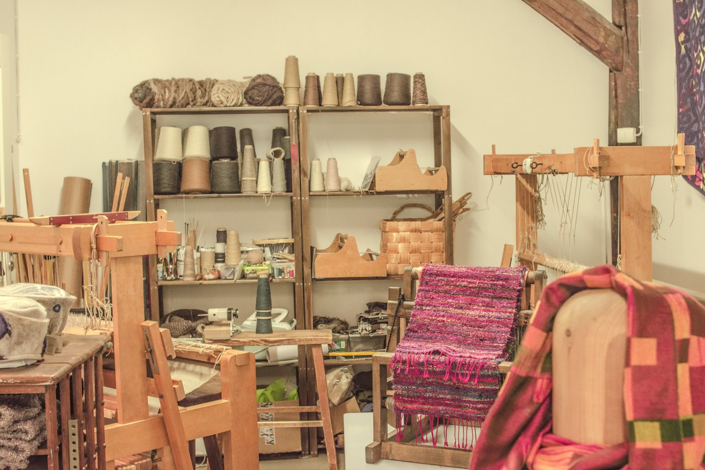 Weaving looms stocked with colorful yarn in a bright textile workshop.