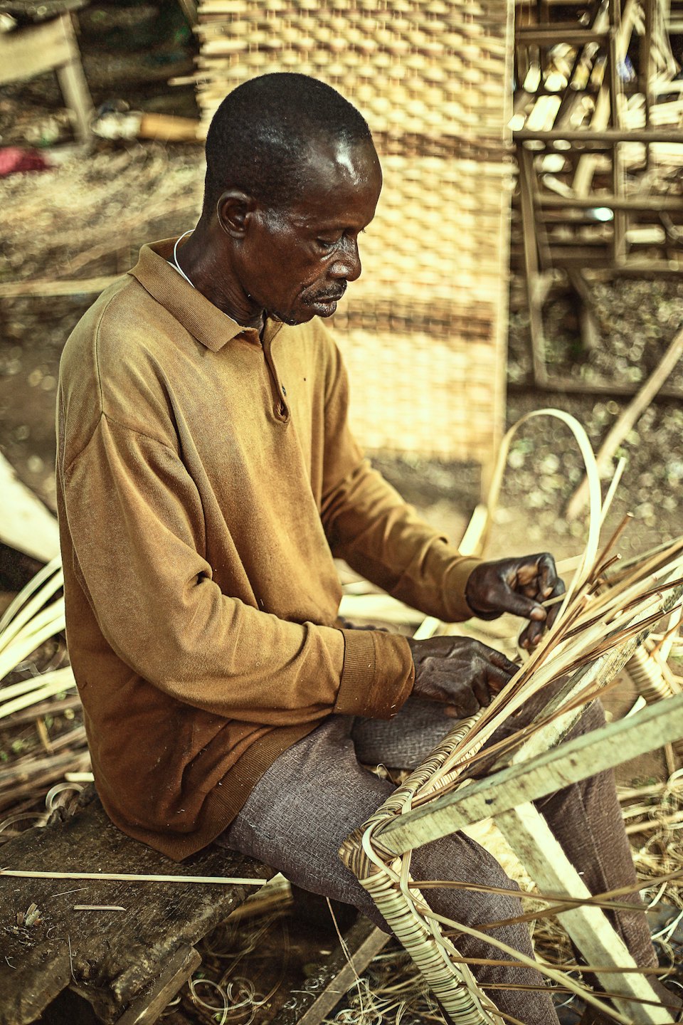 A man weaves natural wicker fibers in an open workshop.