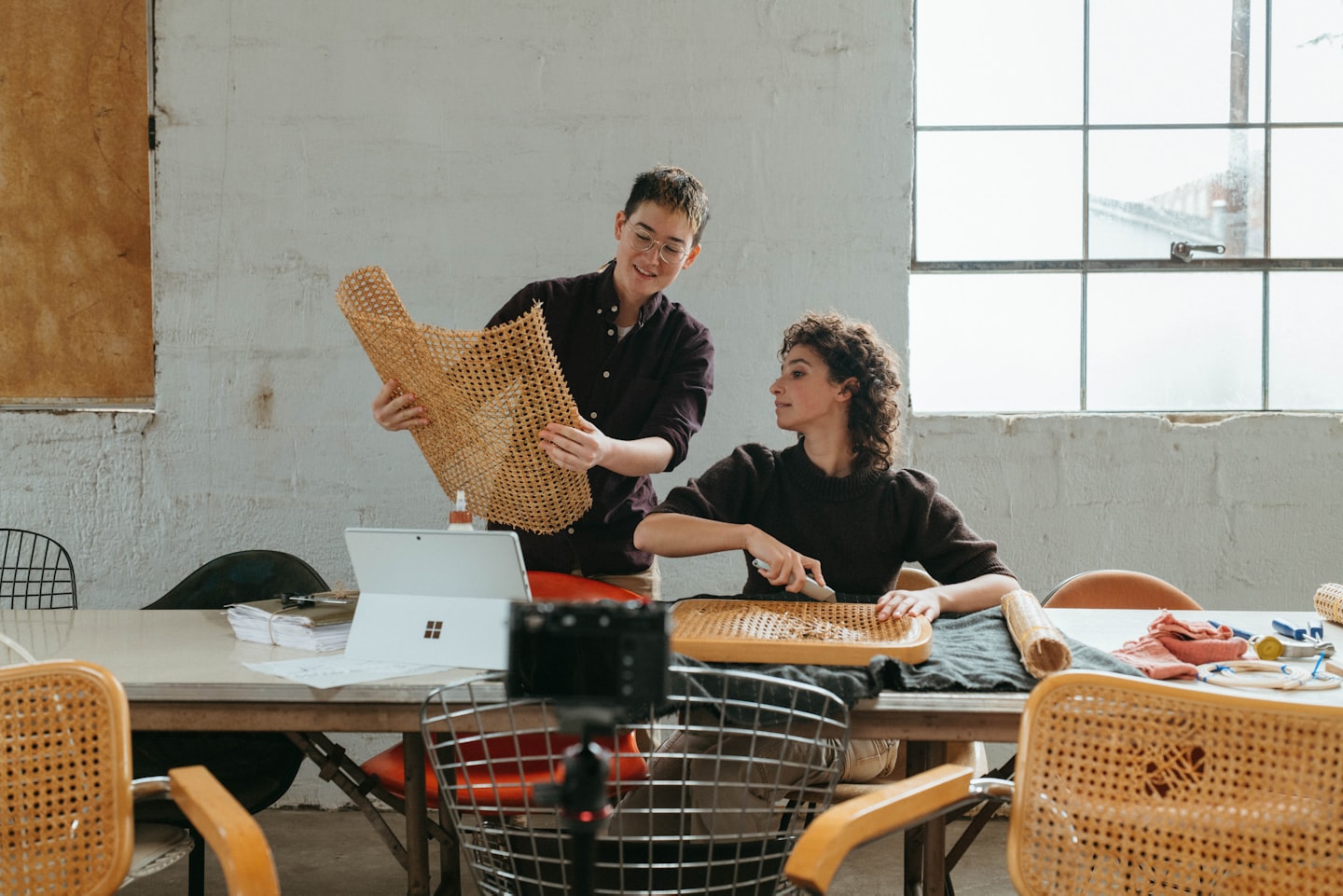 Two people collaborate on woven craft projects in a workshop.