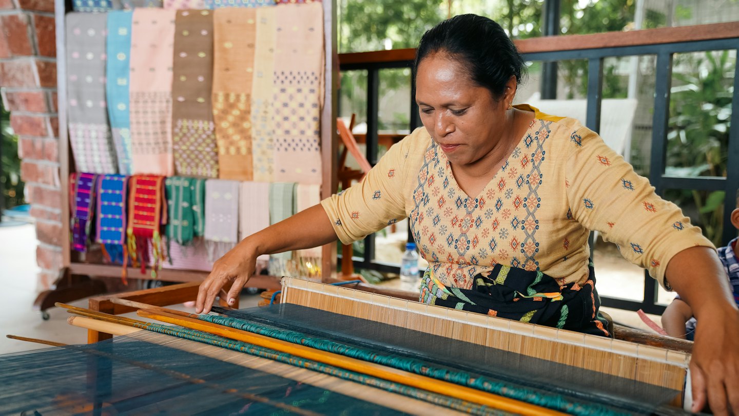 A woman weaves colorful fabric on a traditional wooden loom.